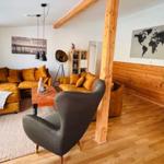 Wohnzimmer mit braunem Sofa, grauer Sessel und Holzboden.