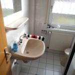Bathroom with sink, toilet, and window with roller blind.