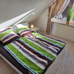 Bedroom with sloped ceiling, bed, nightstand, and window with plant.