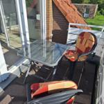 Terrace with table and two chairs, view of garden and house.