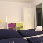 Schlafzimmer mit Doppelbett, Kleiderschrank und bunten Aufbewahrungskästen.