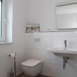 Badezimmer mit Toilette, Waschbecken und Spiegel. Fenster sorgt für Tageslicht.