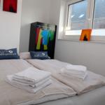 Schlafzimmer mit Bett, Handtüchern und Kleiderschrank. Fenster mit Blick auf Dächer.
