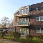 Zweistöckiges Haus mit Balkonen und Garten. Zwei Balkone mit Stühlen. Parkplatz vorne.