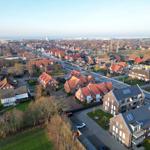 Aerial view of residential area with red-roofed houses and sea in distance.
