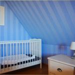 Kinderzimmer mit Kinderbett, Nachttisch und Wandbild an blau gestreifter Wand.