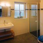 Badezimmer mit Waschbecken, Dusche und Toilette. Fenster mit Seepferdchen-Dekoration.