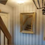 Hausflur mit Streifenwand, Spiegel und Holztreppe