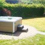 Whirlpool auf Terrasse mit Garten und Liegestuhl im Hintergrund.