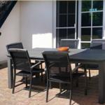 Terrasse mit Tisch und vier Stühlen. Hintergrund: Haus mit Dach und Fenster.