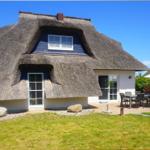 Dorfhaus mit Strohdach, Terrasse und Garten. Weiße Wände und Holzelemente.