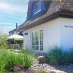 Haus mit Strohdach, weißer Fassade und Gartenbereich mit Sitzgelegenheit.