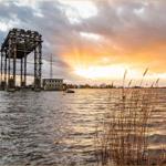 Wasserfläche mit Industrieanlage und Sonnenuntergang.