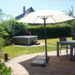 Terrasse mit Tisch, Stühlen und Sonnenschirm. Hintergrund: Whirlpool und grüner Garten.