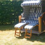 Schwimmbadliege mit blau-weiß kariertem Stoff und Getränkehaltern im Garten.