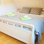 Schlafzimmer mit weißem Bett, Holzboden und zwei Nachttischen mit Lampen.