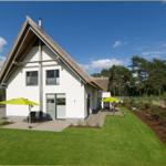 Moderne Villa mit Dachstuhl, Terrasse und Garten. Zwei gelbe Sonnenschirme stehen bereit.
