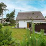 Moderne Villa mit Strohdach und Holzgarage in grüner Umgebung.