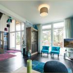 Wohnzimmer mit blauen Sesseln, großen Fenstern und schwarzem Boden