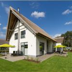 Moderne Villa mit Strohdach, Terrasse und grünem Garten unter blauem Himmel.