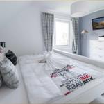 Schlafzimmer mit weißem Bett, Fernseher und Fenster mit Vorhängen.