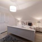 Schlafzimmer mit weißem Bett, Nachttischen und Kleiderschrank unter schrägem Dach.