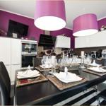 Essbereich mit Tisch, Stühlen und moderner Küche. Violette Wände und hängende Lampen.