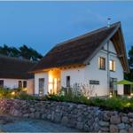 Haus mit strohgedecktem Dach, umgeben von Steinmauer und Bäumen bei Dämmerung.