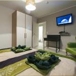 Schlafzimmer mit Bett, grüner Sessel und Wand-TV.