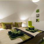 Schlafzimmer mit Dachschräge, Bett mit grünen Kissen und Handtuchblumen.