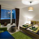 Schlafzimmer mit Bett, grünem Teppich und Fenster mit Vorhängen.