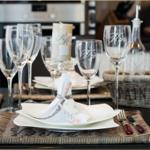 Tisch gedeckt mit Tellern, Gläsern und Besteck auf geflochtenen Untersetzer.