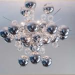 Eine moderne Deckenleuchte mit silbernen Kugeln und Glasbausteinen hängt an der Decke.