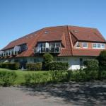 Modernes Mehrfamilienhaus mit Balkonen und rotem Dach unter blauem Himmel.