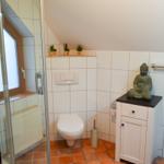 Badezimmer mit Dusche, Toilette und Buddha-Figur auf Schrank.