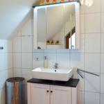 Badezimmer mit Waschbecken, Spiegelschrank und Duschbereich unter Dachschräge.