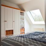 Schlafzimmer mit Dachfenster, weißem Schrank und gefüttertem Bett.
