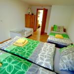Zwei Betten mit grün-weißem Bettzeug und gelben Handtüchern. Ein Kinderbett und ein Schrank sind sichtbar.