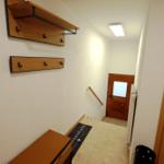 Eingangsbereich mit Holzregal, Bank und Tür mit Glasfenster.