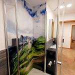 Duschkabine mit Berglandschaftsbild, Duschbrause und integriertem Regenduschkopf.