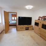 Wohnzimmer mit Fernseher, Holzmöbeln und Blick in Schlafzimmer.