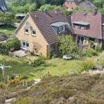 Haus mit Garten, Terrasse und kleinem Holzschuppen. Umgeben von Bäumen und Grünflächen.