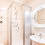 Badezimmer mit Dusche, Waschbecken und runden Spiegel.