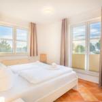 Schlafzimmer mit Doppelbett, zwei Fenstern und Terrasse.