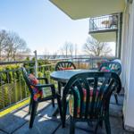Terrasse mit Tisch und Stühlen, Blick auf Wasser und Bäume.