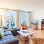 Wohnzimmer mit Sofa, Couchtisch und Fernseher. Blick auf Balkon mit Garten.