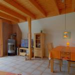 Wohn- und Essbereich mit Holzdecke, Esstisch, Kaminofen und Terrassentür.