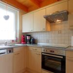 Küche mit Holzschränken, Spüle, Herd und Backofen. Fenster mit Herzschmuck.