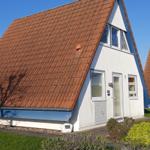Ein Haus mit rotem Dach und weißer Fassade. Garten und kleiner Anbau sind sichtbar.