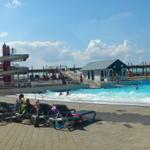 Poolbereich mit Rutschen und Liegestühlen unter blauem Himmel.